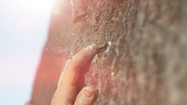 SLOW MOTION, LENS FLARE, MACRO, DOF: Woman grabs a crimp hold while scaling a challenging cliff. White magnesium powder flies in the air as rock climber scales a cliff and places fingers onto an edge.