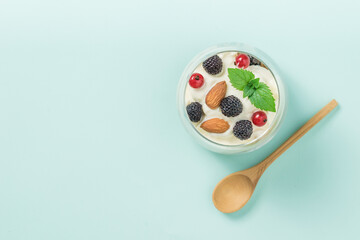 Wooden spoon next to a glass of yogurt, granola, berries and almonds on a blue background.
