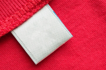 White blank laundry care clothes label on red cotton shirt background