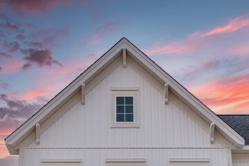 New gable with decorative brackets, white vertical vinyl lap siding with square attic window on a...