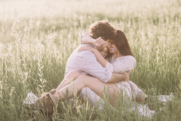 Man kisses his girlfriend sitting on a grass.