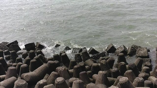 Closeup of back bay small water splashes along the Marine Drive rocks during a bright, hot day in Mumbai India, slow motion shot.