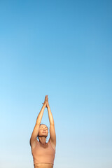 Young beautiful woman is meditating with raised hands against the sky. The girl raises her hands to heaven in prayer. Calmness and harmony.