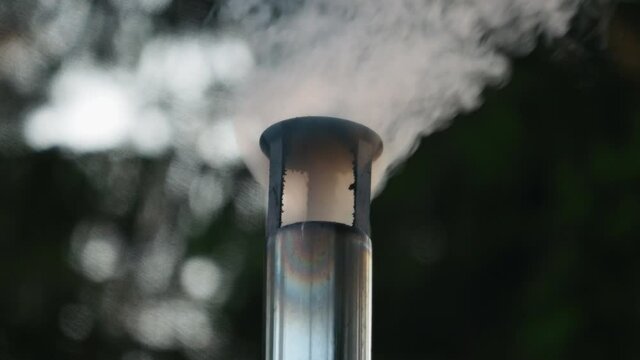Close view of smoke comes out of a stove chimney in the forest.