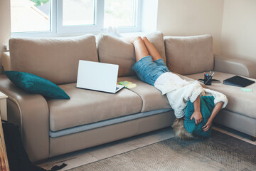 Exhausted caucasian blonde woman lying on the couch while working at the laptop with some folders