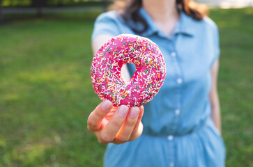 Female hand holding pink sweet donut. Diet, unhealthy food, cooking concept. Close up, copy space