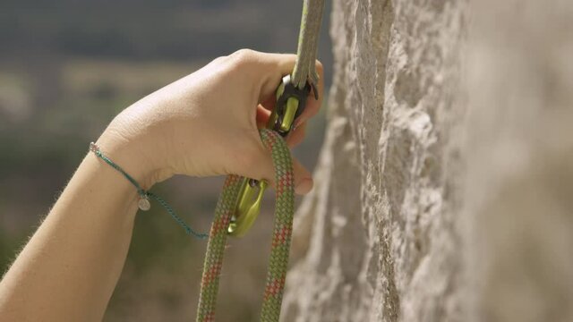 SLOW MOTION, CLOSE UP, DOF: Fit woman top roping loops her rope into a safety carabiner. Unrecognizable female rock climber clips her belay rope into a carabiner. Girl top roping up challenging cliff