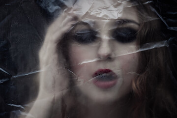 Young beauty sad woman trapped behind a plastic sheet as protection against COVID-19. Nicely fits for book cover