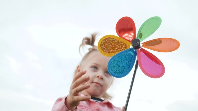 little daughter girl play pinwheel a lifestyle wind toy. happy family concept. child plays with windmill. portrait girl blonde kid holds flower toy spinning pinwheel. happy childhood