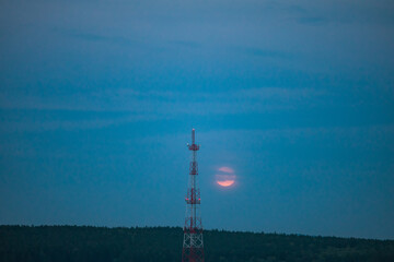 Obraz premium Communication tower against the night sky with a large red moon.