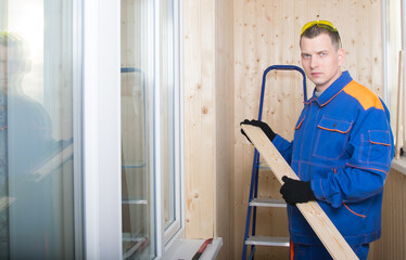 master in blue uniform, on the decoration of the premises, holds a wooden wall cladding