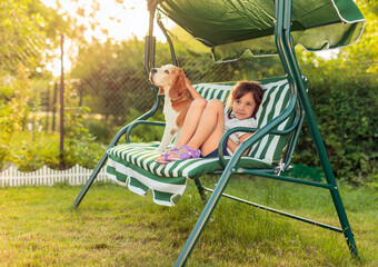 Little girl is resting on a bench with her dog.