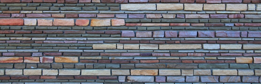 Surface and texture of multy-colored (colorful) decorative stone wall, background. Varicolored flat stones of regular shape in the wall construction. Stylish decorative stone laying. Panorama
