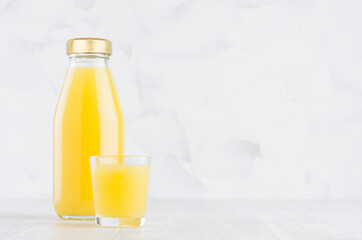 Fresh orange juice in glass bottle mock up with wine glass on wood table in soft light white interior, template for packaging, advertising, design product, branding identity.