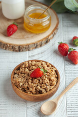 Homemade granola in a wooden bowl with strawberries and honey on wooden background. The concept of a healthy Breakfast.