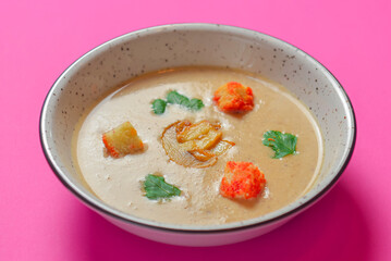 Creme soup with mushrooms served in a white bowl isolated on bright pink background. Copy space banner.