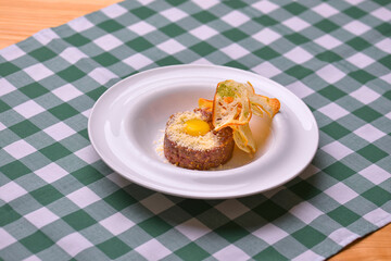 Close up of beef tartar with capers and small toasts. Served on a white plate over green plaid tablecloth background.