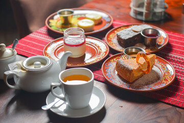 Table set for tea time with sweet desserts. Chocolate brownie cake, vanilla cake, panna cotta. Tea pot with sweet tea.