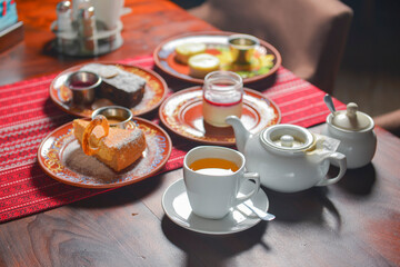 Table set for tea time with sweet desserts. Chocolate brownie cake, vanilla cake, panna cotta. Tea pot with sweet tea.