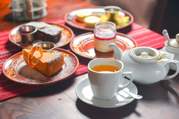 Table set for tea time with sweet desserts. Chocolate brownie cake, vanilla cake, panna cotta. Tea pot with sweet tea.