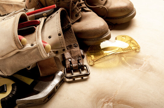 Construction concept background of toolbelt yellow boots goggles ant tools on plywood