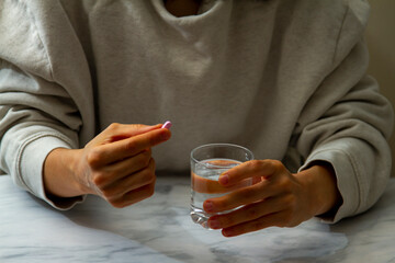 A woman is seen as she is holding a pill in one hand and a glass of water on the other hand. She is...