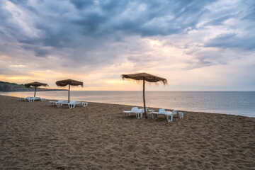 Straw sunshades and sunbeds on the empty sandy beach with sea in the background before sunset