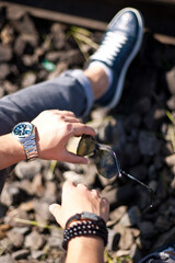 Fashion portrait of young businessman handsome model man in casual cloth suit with accessories on hands, steel watches,grey jeans and bracelets