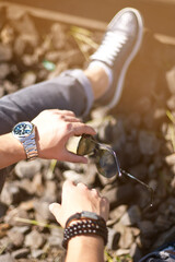 Fashion portrait of young businessman handsome model man in casual cloth suit with accessories on hands, steel watches,grey jeans and bracelets.