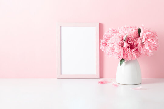 Home interior floral decor with pink peonies on shelf. Front view blank mock up of photo frame. Beautiful flowers pink peonies in vase on white background.