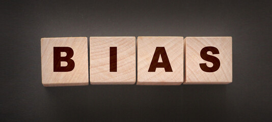 The word BIAS, spelt with wooden letter tiles over a black background