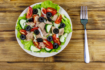 Tasty tuna salad with lettuce, black olives and fresh vegetables on wooden table. Top view