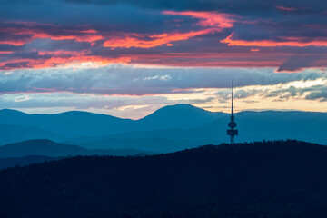 Canberra tower with colourful sunset and layers of clouds and mountains in the background - obrazy, fototapety, plakaty