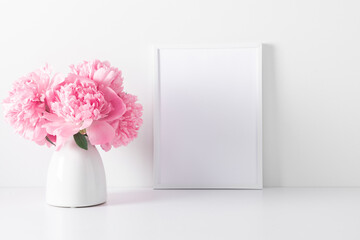 Home interior floral decor with pink peonies on white shelf. Front view blank mock up of photo frame. Beautiful flowers pink peonies in vase on white background © prime1001