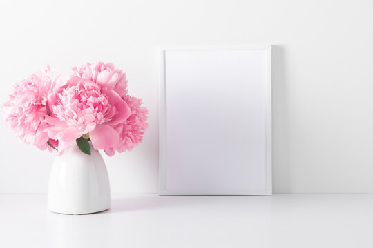 Home interior floral decor with pink peonies on white shelf. Front view blank mock up of photo frame. Beautiful flowers pink peonies in vase on white background