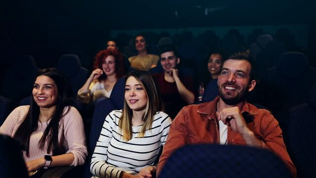 Group of cheerful people laughing while watching movie in cinema.