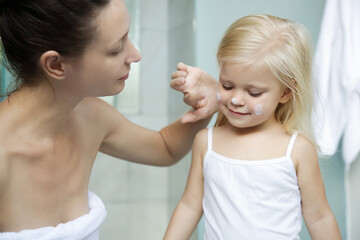 Obraz na płótnie Canvas Mom applying cream on her daughter face in bathroom. 