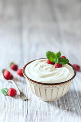 Greek yogurt in a ceramic bowl on a light wooden table.