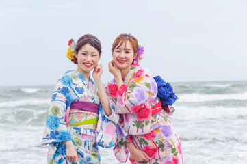 海をバックに散歩する二人の浴衣の女性