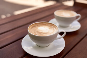 Two cups of cappuccino on the wooden background. Beautiful brown foam, white ceramic cups, place for text