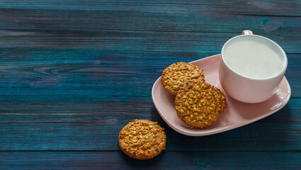 Oatmeal raisin nut cookie and pink cup of coffee with milk on wooden background