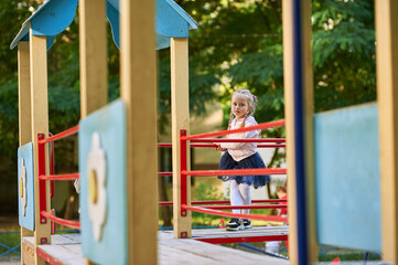 a little girl with blond hair plays on the playground and climbs on the game slides and steps of...