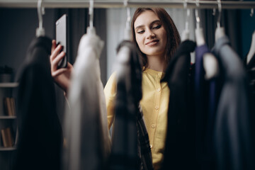 Front view of female fashion expert standing in wardrobe full of stylish clothing and filming video...