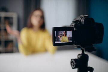 Close up of digital video camera with cheerful woman in yellow sweater and eyeglasses on screen....