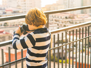 Blonde caucasian boy with vintage binoculars exploring the city from his flat balcony