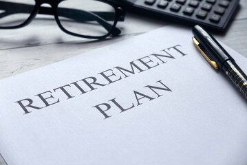 Selective focus of glasses,calculator,pen and paper written with Retirement Plan on white wooden background.