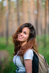 Portrait of a woman with long hair and backpacks Hiking in a pine forest, tourism and banner for healthy recreation, copy space