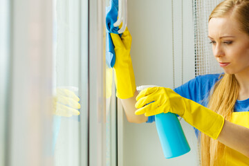 Girl cleaning window at home using detergent rag