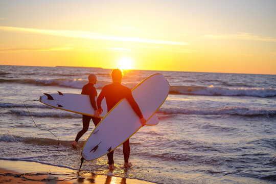 Unrecognizable surfers entering waving sea