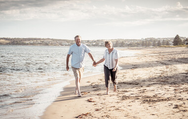 Healthy active senior couple holding hands, embracing each other and walking on beach